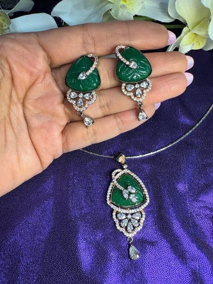 A classic combination of emerald green and sparkling stones. This pendant set features a rich green carved stone in a triangular design, perfect for adding a pop of color and elegance to your ensemble.