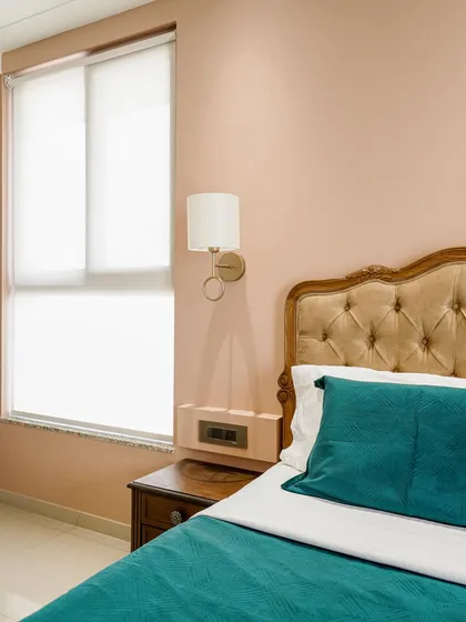 A bedroom with a classic button-tufted headboard, soft pink walls, and teal bedding for a pop of color.