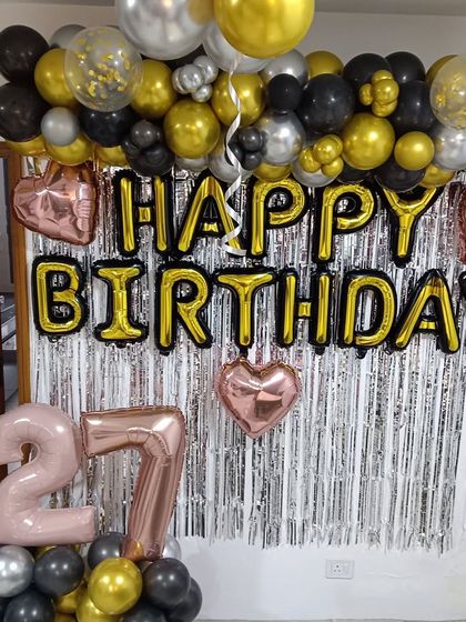 A classic at-home birthday decoration with a silver tinsel curtain. I added a "Happy Birthday" foil banner, a garland of black, gold, and silver balloons, and rose gold foil balloons for the age '27'.