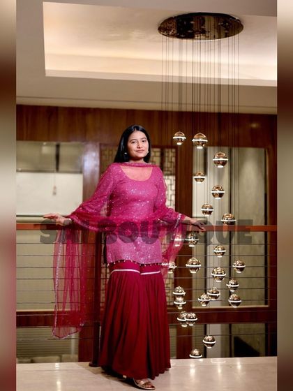A client looking elegant in a pink and red sharara suit with a net cape. A perfect outfit for a sangeet or reception.