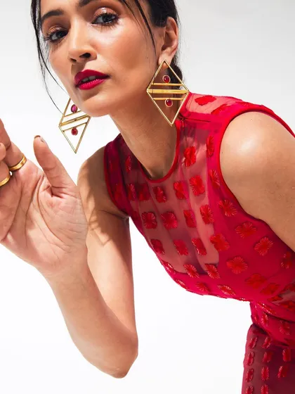 An engaging close-up from the red dress studio shoot. The model leans in towards the camera, showing off the geometric earrings and bold red lip, creating a confident and compelling fashion portrait.