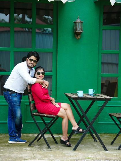 A cool and casual pose at an outdoor cafe set, with a vibrant green wall in the background.