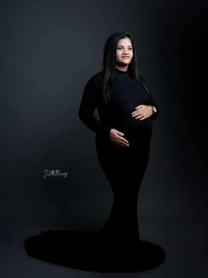 A powerful and elegant full-length portrait in a black gown with a long train. The dramatic lighting and strong pose create a timeless and iconic image of motherhood.