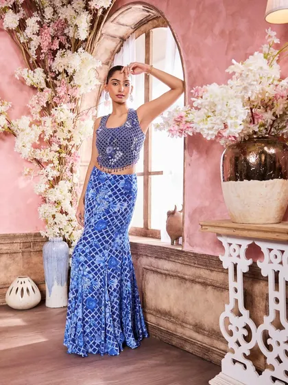 A full-length shot of a model in a stunning blue printed lehenga. The makeup is elegant and polished, with a sleek updo to highlight the intricate neckline of the blouse.