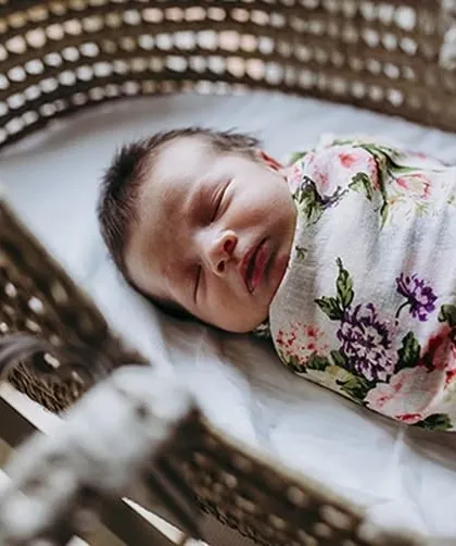A serene shot of a newborn sleeping peacefully in a bassinet, swaddled in a floral blanket. These classic newborn portraits are timeless.