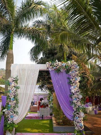 A beautiful entrance arch decorated with lavender drapes and arrangements of white and blue flowers. It creates a soft and welcoming pathway into the garden ceremony area.