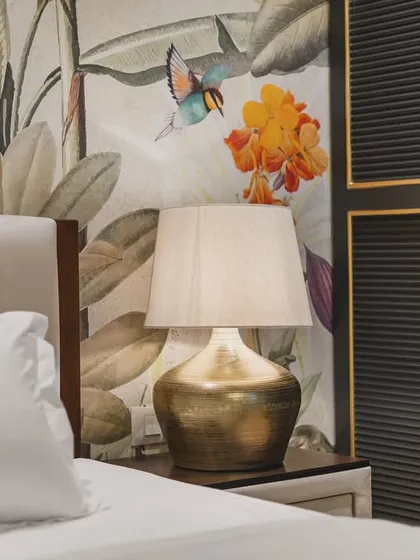 A close-up detail of a bedroom sanctuary, where a bold, tropical wallpaper becomes a work of art. The interplay of the warm, metallic lamp base, the soft textures of the bedding, and the intricate design of the wardrobe door showcases my focus on capturing the small details that create a room's character.