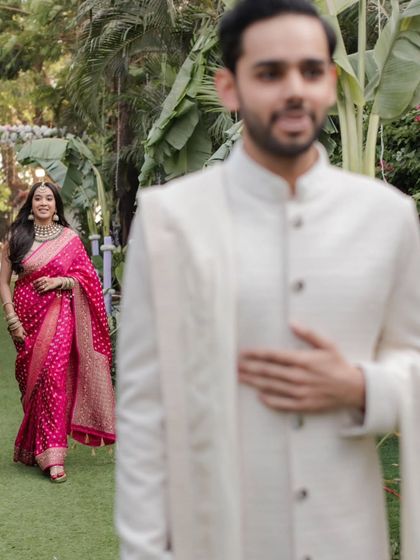 An artistic shot capturing the anticipation of the 'first look', with the groom in the foreground and the bride walking towards him.