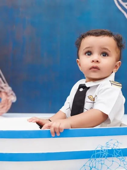 A curious little sailor peeks out from his boat prop during his nautical-themed first birthday shoot.