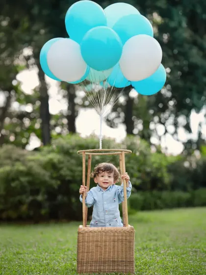 A charming outdoor portrait featuring the popular hot-air balloon prop. The lush green background and bright blue balloons make for a vibrant and cheerful photograph.
