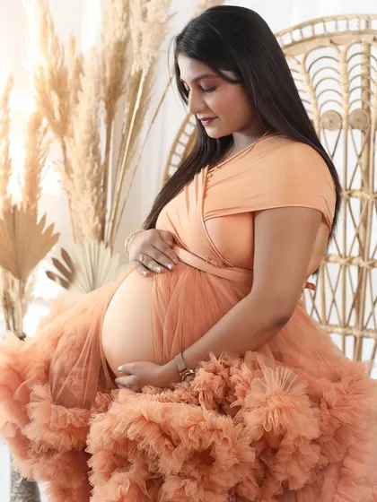 A beautiful close-up capturing the feeling of a lifetime. The focus is on the baby bump, tenderly held, framed by a gorgeous peach ruffled gown.