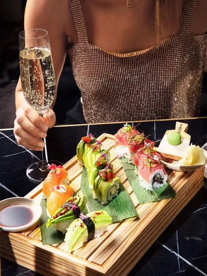 A lifestyle shot featuring a beautiful sushi platter and a glass of champagne at Akina Mumbai. This image is about selling an experience: sophisticated dining, exquisite food, and a touch of glamour.