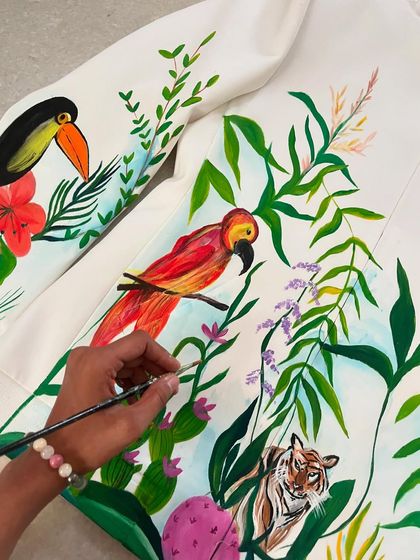 A work-in-progress shot of a forest-themed jacket. Here, I'm painting a toucan, a parrot, and a tiger cub among tropical leaves, building the scene layer by layer.