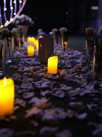 The same romantic pathway seen at night. The candles create an even more intimate and magical atmosphere, with their warm light reflecting off the scattered petals.