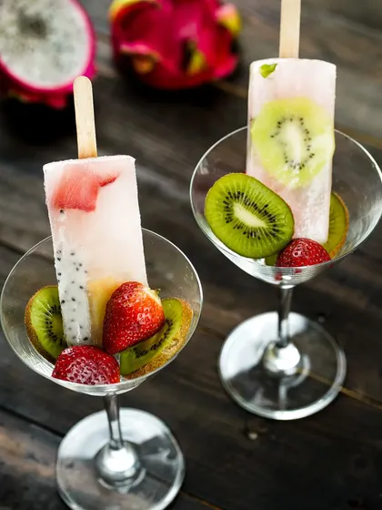 Gourmet fruit popsicles served elegantly in martini glasses with fresh kiwi and strawberries, elevating them from a simple treat to a sophisticated dessert.