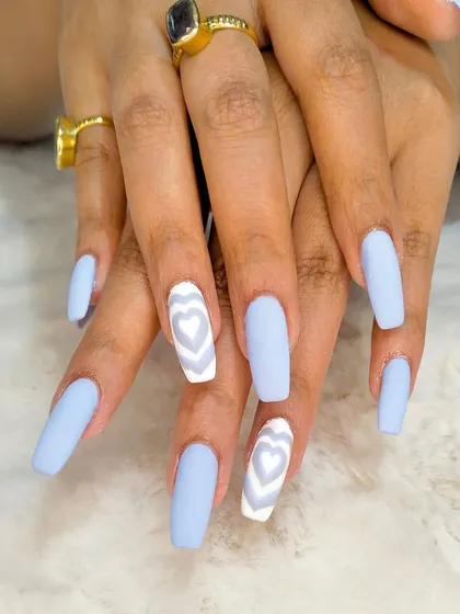 A trendy and playful design featuring long, matte sky-blue nails with a creative white-on-white layered heart design on the accent nails.