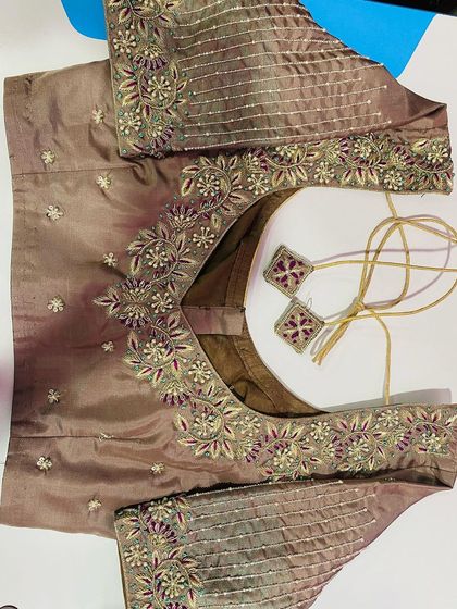 A muted brown blouse with delicate floral embroidery. The sleeves have fine lines of stitching to create a textured pattern.