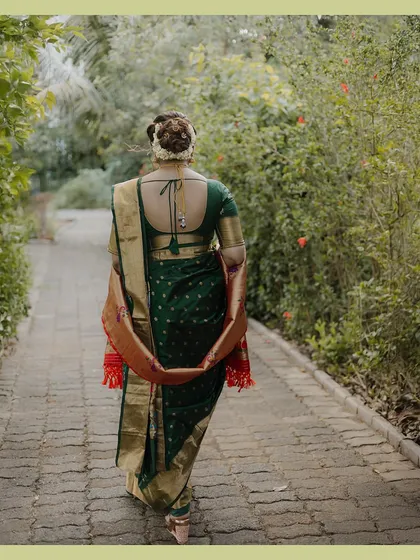 A full-back shot of the bride walking down a path, showcasing the elegant drape of her saree and her traditional hairstyle adorned with flowers.