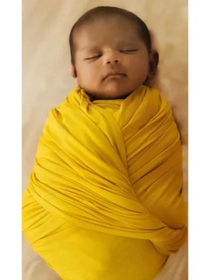 A tiny newborn is swaddled tightly in a bright yellow wrap, looking like a little ray of sunshine.