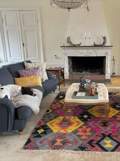 We love seeing our pieces in our clients' homes around the world. Here, our vibrant, multicolored dhurrie-style carpet and assorted cushions add a bold, eclectic touch to a classic European living room.