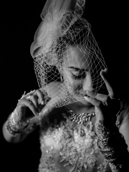 A dramatic black and white bridal portrait with a birdcage veil. The use of shadow and light creates a classic, film noir-inspired mood.
