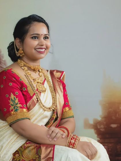 A radiant solo portrait of a woman dressed in a traditional white and red saree with ornate gold jewelry.