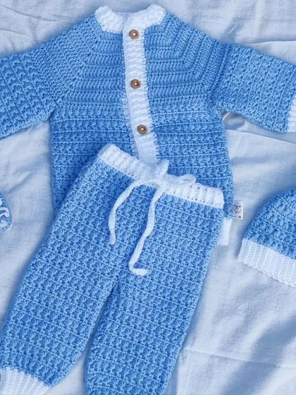 A complete newborn baby winter set in soft blue and white yarn. The set includes a cozy cardigan, pants with a drawstring, a pom-pom hat, and adorable little booties.