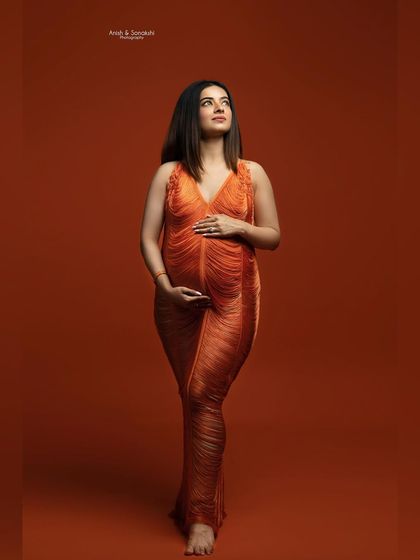 Bold and beautiful in burnt orange. This full-length portrait against a matching solid backdrop makes a vibrant and modern statement, highlighting the gorgeous silhouette of the baby bump.