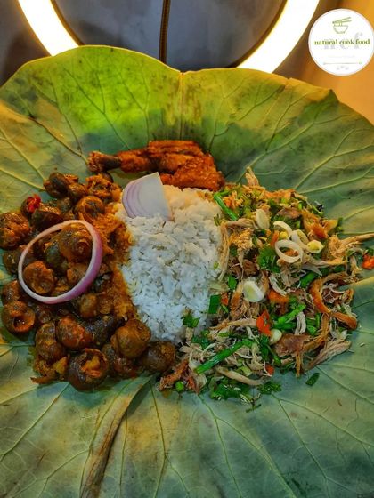 A unique platter served on a lotus leaf, featuring my chicken spicy salad, river snails, sticky rice, and a fried chicken drumstick.