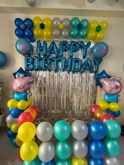 A simple and sweet Peppa Pig decoration for a home party. This setup includes character foil balloons and a colorful balloon arrangement against a silver fringe backdrop.