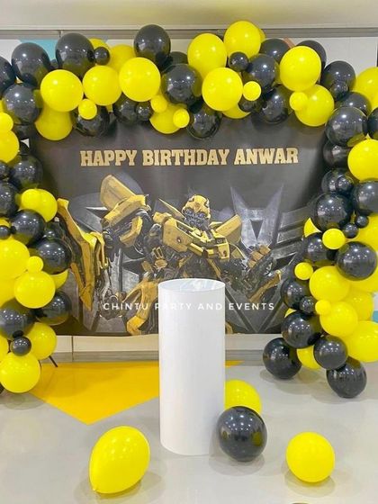 A striking Bumblebee from Transformers themed birthday decoration. The setup uses a bold yellow and black balloon arch framing a character backdrop.