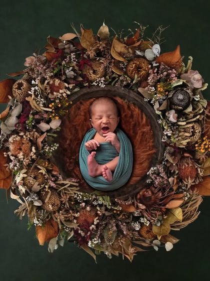 A perfect yawn from a newborn swaddled in teal, nestled within a wreath of dried autumn flowers and leaves. This overhead shot is both artistic and authentic.