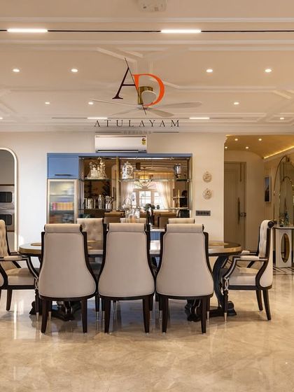 A grand dining room in a neo-classical style, featuring a large dining table, upholstered chairs, and a coffered ceiling with modern track lighting.