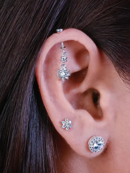 This elegant ear stack features a floral drop hanging from an industrial piercing, complemented by a matching floral stud on the lobe. It's a perfect example of a coordinated, feminine style.