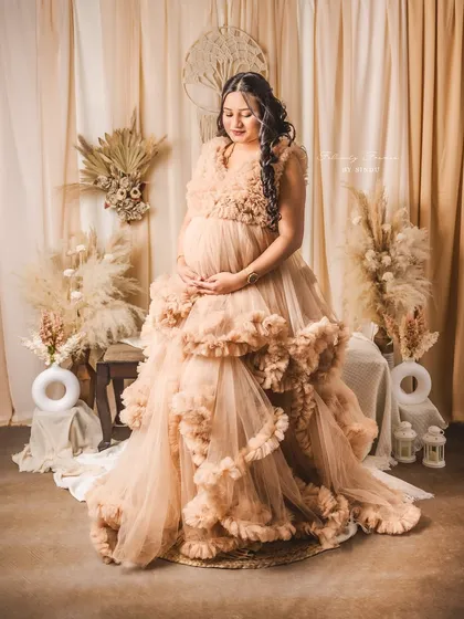 An expectant mother looking serene in a stunning, ruffled beige gown. This image highlights my boho-chic studio maternity sessions, complete with pampas grass and soft, natural styling.