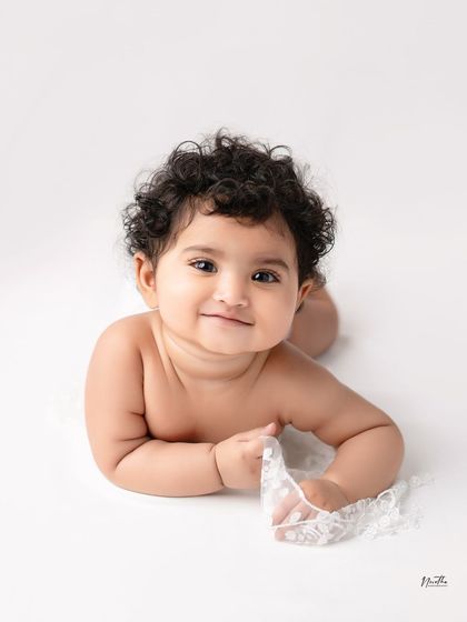 A simple and beautiful portrait of a baby with curly hair, lying on a white surface.