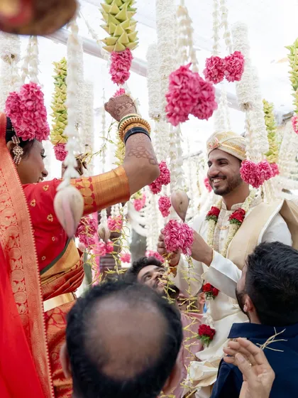 A candid moment of joy between the bride and groom under the floral canopy. The hanging strings of jasmine and pink carnations create a beautiful, interactive element for the couple and their guests.