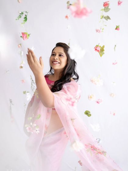 A moment of pure bliss. The mom-to-be looks up, catching falling flowers with a happy smile, creating a dynamic and joyful image that feels so full of life.