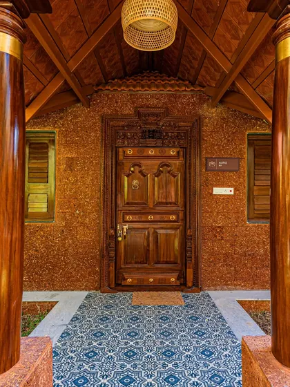 Detail is everything in architecture. This intricately carved wooden door, set against a rustic laterite brick wall and framed by traditional pillars, creates a grand and welcoming entrance for a resort project. It's a nod to timeless Indian craftsmanship.