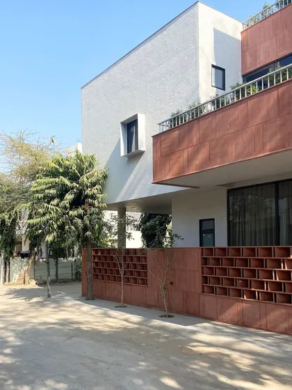 An angled perspective of the Jaipur residence, showing the relationship between the solid upper volume, the open terrace, and the protective jali screen. The design prioritizes both privacy and a connection to the outdoors.