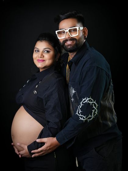 A happy and relaxed couple's portrait. Their coordinated black outfits and genuine smiles create a modern and stylish memory of their pregnancy.
