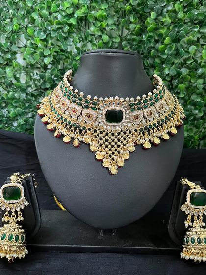 This stunning green and gold kundan choker set is a popular rental choice for mehendi or reception events. The set includes a broad necklace and heavy jhumkas, all adorned with emerald-green stones.