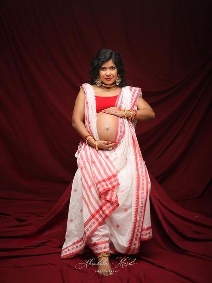 A proud and beautiful portrait of a mother-to-be in a traditional Bengali saree, her hands lovingly placed on her bump.