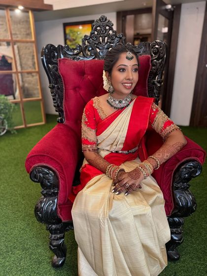 My beautiful bride Preethi seated elegantly for her engagement photos. She wears a classic off-white and red saree, with her makeup kept fresh and radiant to match her diamond jewellery.