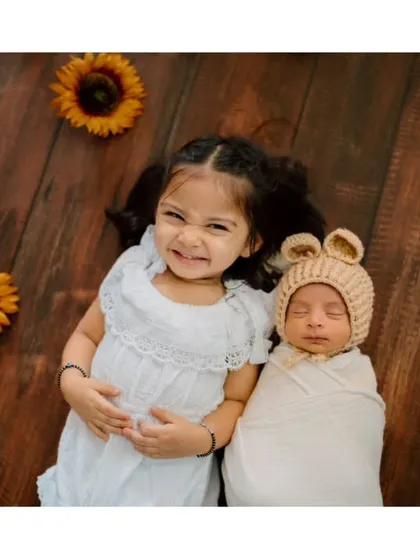 A slightly different angle of the siblings lying on a rustic wood floor surrounded by sunflowers. The sister's proud expression says it all.