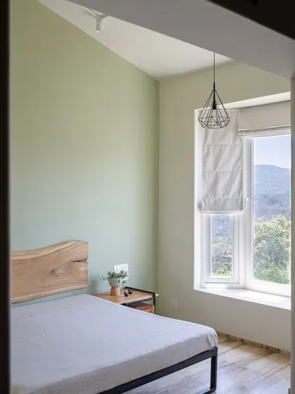 This bedroom uses a live-edge wood headboard as a natural, artistic focal point. The sage green wall and simple pendant light create a calm and soothing atmosphere, with the window offering a beautiful view of the hills.