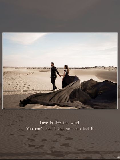 A dramatic scene in the Jaisalmer desert, with the couple standing together as the bride's long black gown flows in the wind across the sand dunes.