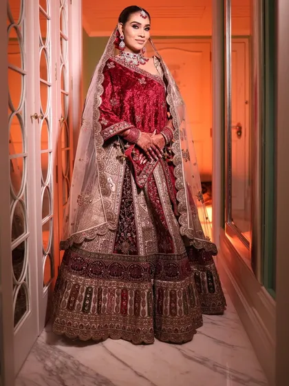 A breathtaking full-length view of a bride in a red velvet lehenga. The lighting highlights the sparkle of the diamond and ruby Polki set, creating a look worthy of royalty.