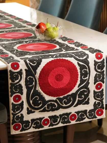 A bold red, black, and white embroidered table runner elegantly laid out on a dining table. The striking pattern and rich colors make it a statement piece for any dining setting.