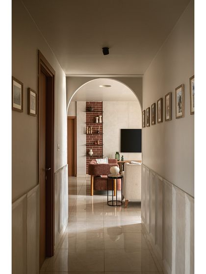 Looking from the corridor back towards the living area, an archway frames the view of the exposed brick wall. The walls of the passage are lined with the family's travel photos, turning a simple hallway into a personal gallery.